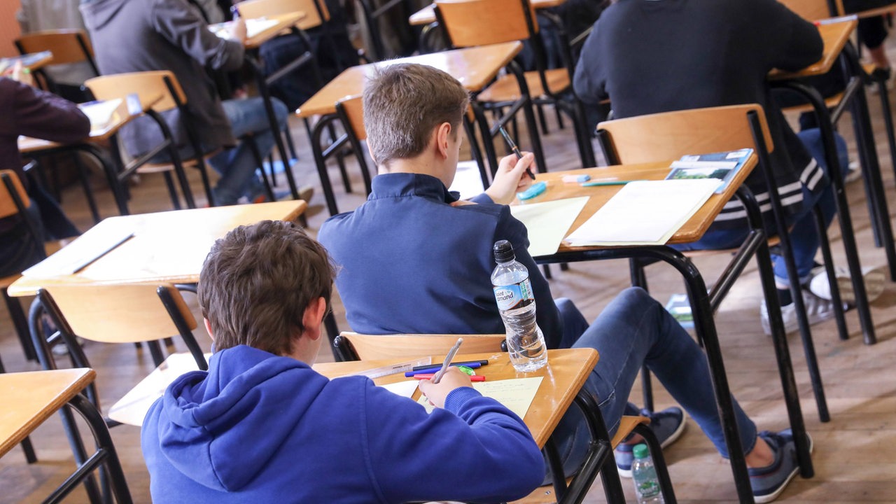 Schüler sitzen hintereinander an Tischen und lösen Aufgaben.