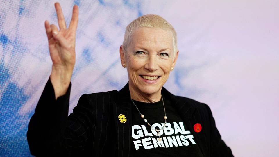 Porträt von Annie Lennox mit Victory-Pose und T-Shirt: "Global Feminist"