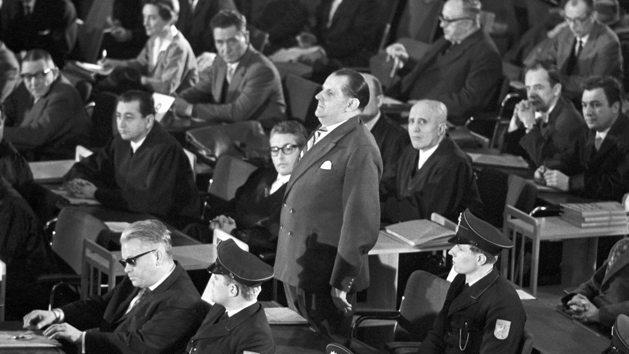 Eröffnung des Auschwitzprozess 1963 in Frankfurt. Das Bild zeigt die Reihe der Angeklagten mit ihren Verteidigern und den wachhabenden Polizisten. 