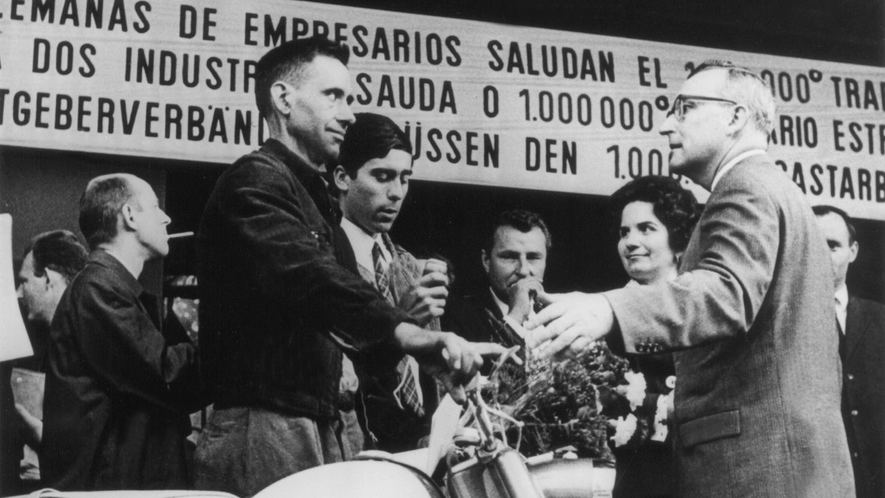 Mit stolzer Miene steht der millionste Gastarbeiter in der Bundesrepublik, Armando Rodrigues (l) aus dem kleinen Dorf Vale de Madeiros in Portugal, neben dem Moped, das er bei seiner Ankunft am 10.09.1964 im Köln-Deutzer Bahnhof geschenkt bekam. 