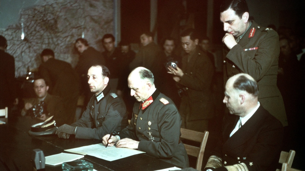 Generaloberst Alfred Jodl (m) unterzeichnet die Kapitulation, sein Adjudant Oberst Wilhelm Oxenius, Admiral Hans Georg von Friedeburg,